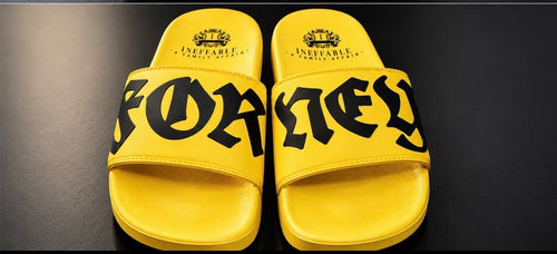 A pair of bright yellow slide sandals with bold black gothic-style lettering across the straps, displayed on a dark reflective surface. The city name 'FORNEY' is prominently printed on the straps, with 'INEFFABLE' and a crown logo visible on the footbeds.